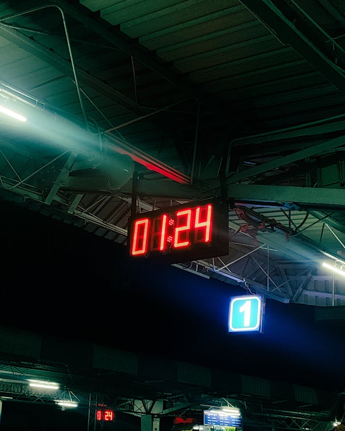 A digital clock showing 01:24 at a dimly lit train station at night.