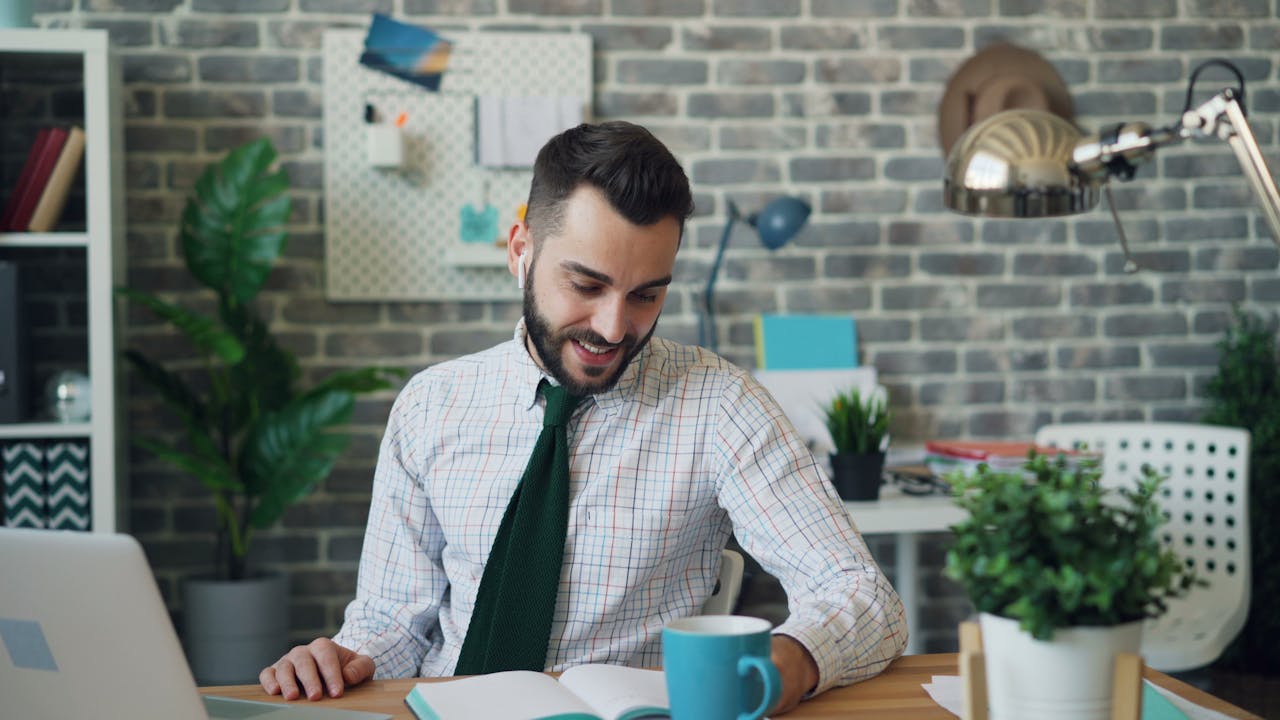 Smiling man in office with laptop and coffee, working efficiently.