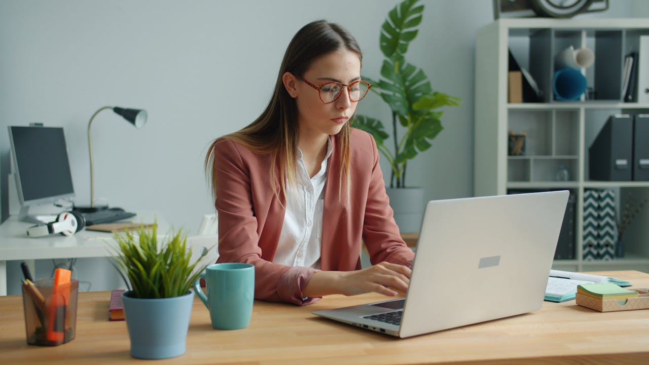 about-img Focused professional woman using a laptop in a modern office setting.